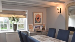 A dining area with a table set for six, a potted plant, framed pictures, and a wall-mounted light fixture.