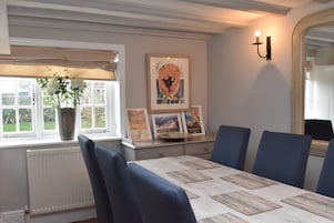 A dining area with a table set for six, a potted plant, framed pictures, and a wall-mounted light fixture.