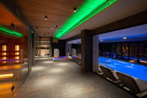 A modern indoor swimming pool area with lounge chairs, a reception desk, and a glass wall. - Hotel Beskid Balneo Medical Resort & SPA (Piwniczna-Zdroj)