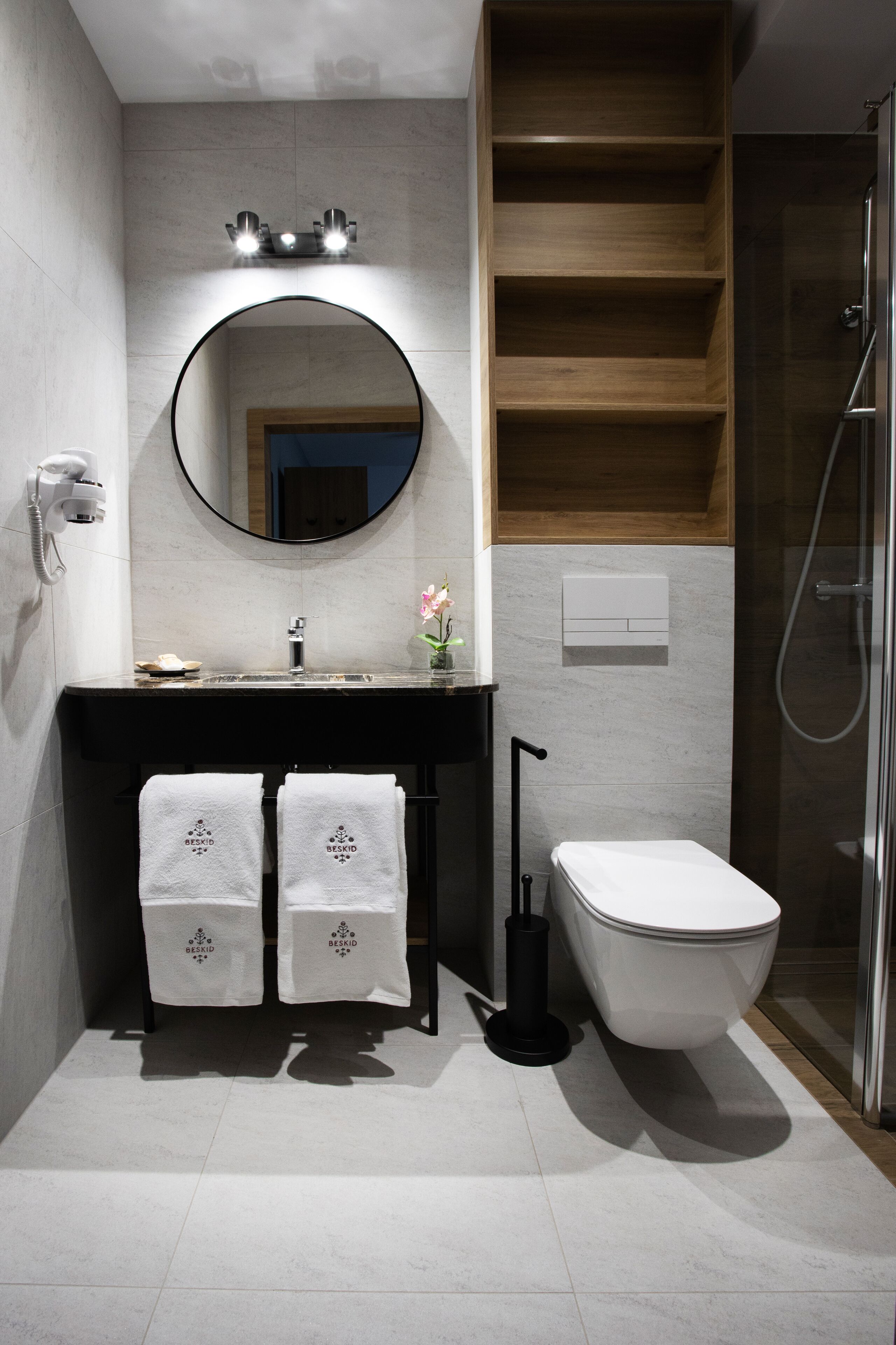 A modern bathroom with a freestanding bathtub, a round mirror, and a wooden shelf above the sink.