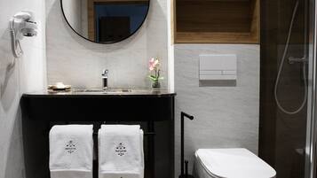 A modern bathroom with a freestanding bathtub, a round mirror, and a wooden shelf above the sink.
