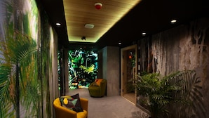 A hallway with a mural, a green armchair, a potted plant, and a wooden ceiling. - Hotel Beskid Balneo Medical Resort & SPA (Piwniczna-Zdroj)