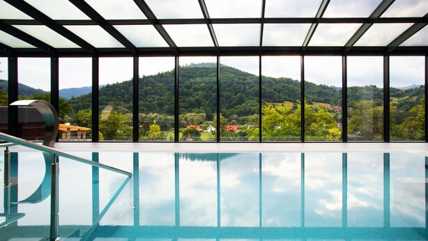 A swimming pool with a view of a mountainous landscape through large windows. - Hotel Beskid Balneo Medical Resort & SPA (Piwniczna-Zdroj)