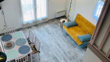 Un vaste espace de vie comprenant un canapé jaune, une table ronde avec des chaises et un escalier.