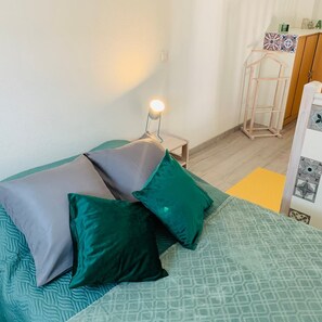 A neatly made bed with green and grey bedding, a bedside lamp, and a small wooden nightstand.