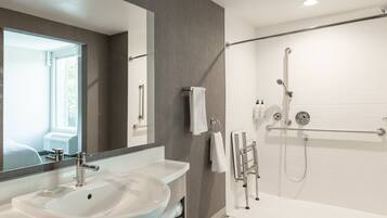 A modern bathroom with a large mirror, a white sink, and a walk-in shower.