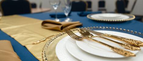 Une table dressée avec des couverts en or et des assiettes blanches, une nappe bleue et une serviette en tissu dorée.