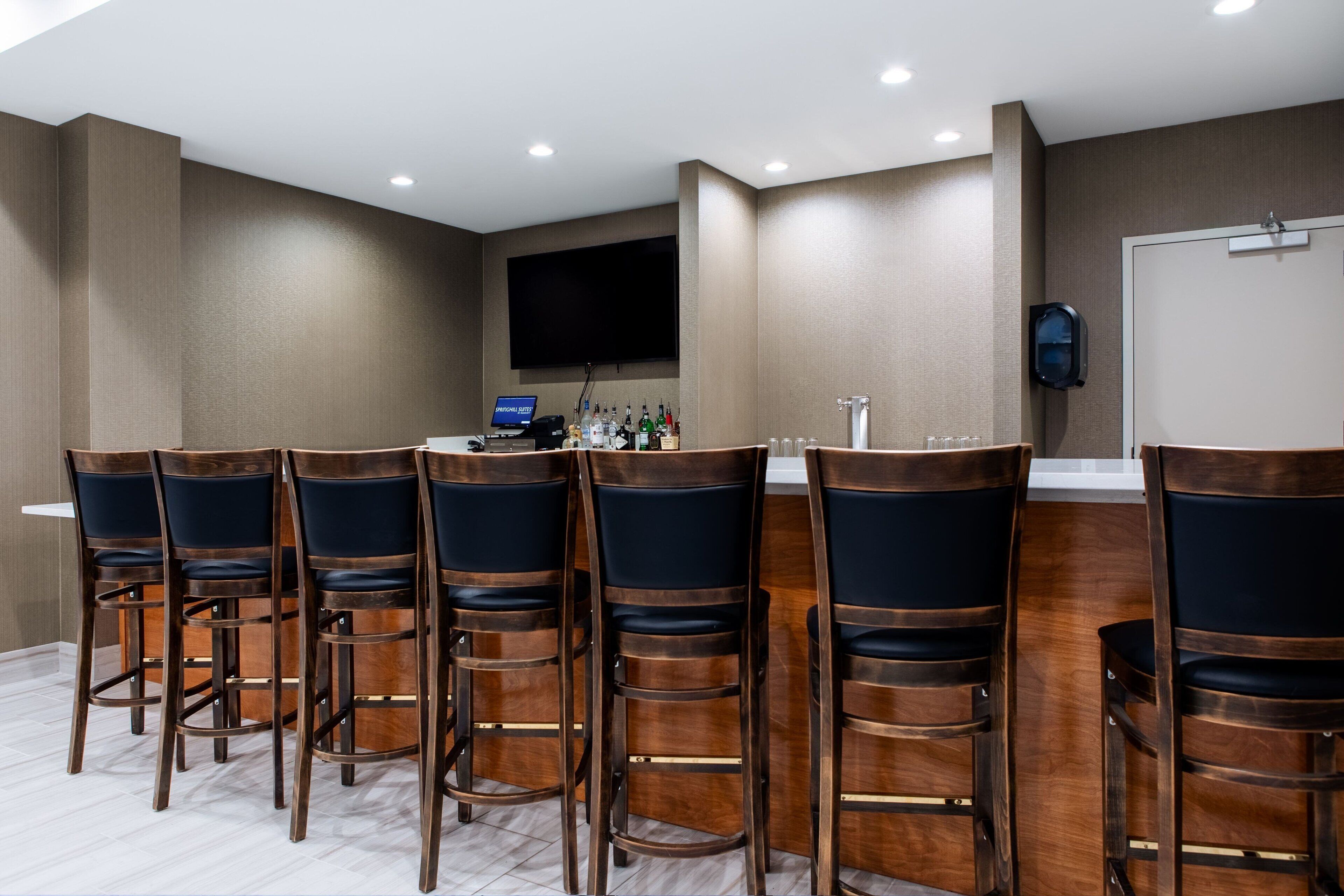 Un espace bar avec des tabourets de bar en bois et un téléviseur à écran plat fixé au mur.