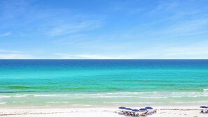 A beach with clear turquoise water and a white sandy shore. There are several blue umbrellas and lounge chairs. - Kings View|Private Beach Access|Gulf Front Home with Stunning Gulf Views (Destin)