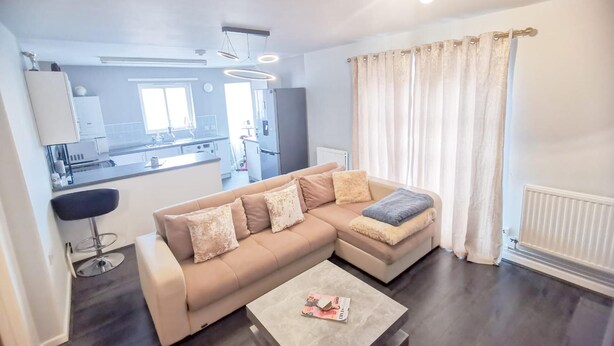 Una sala de estar moderna con un sofá seccional color beige, una mesa de centro y vistas a una cocina y comedor.