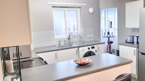 Una cocina moderna con lavadora incorporada, refrigerador de acero inoxidable y ventana que proporciona luz natural.