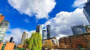 Un paisaje urbano con edificios modernos, una mezcla de estilos arquitectónicos y un cielo azul despejado con nubes.