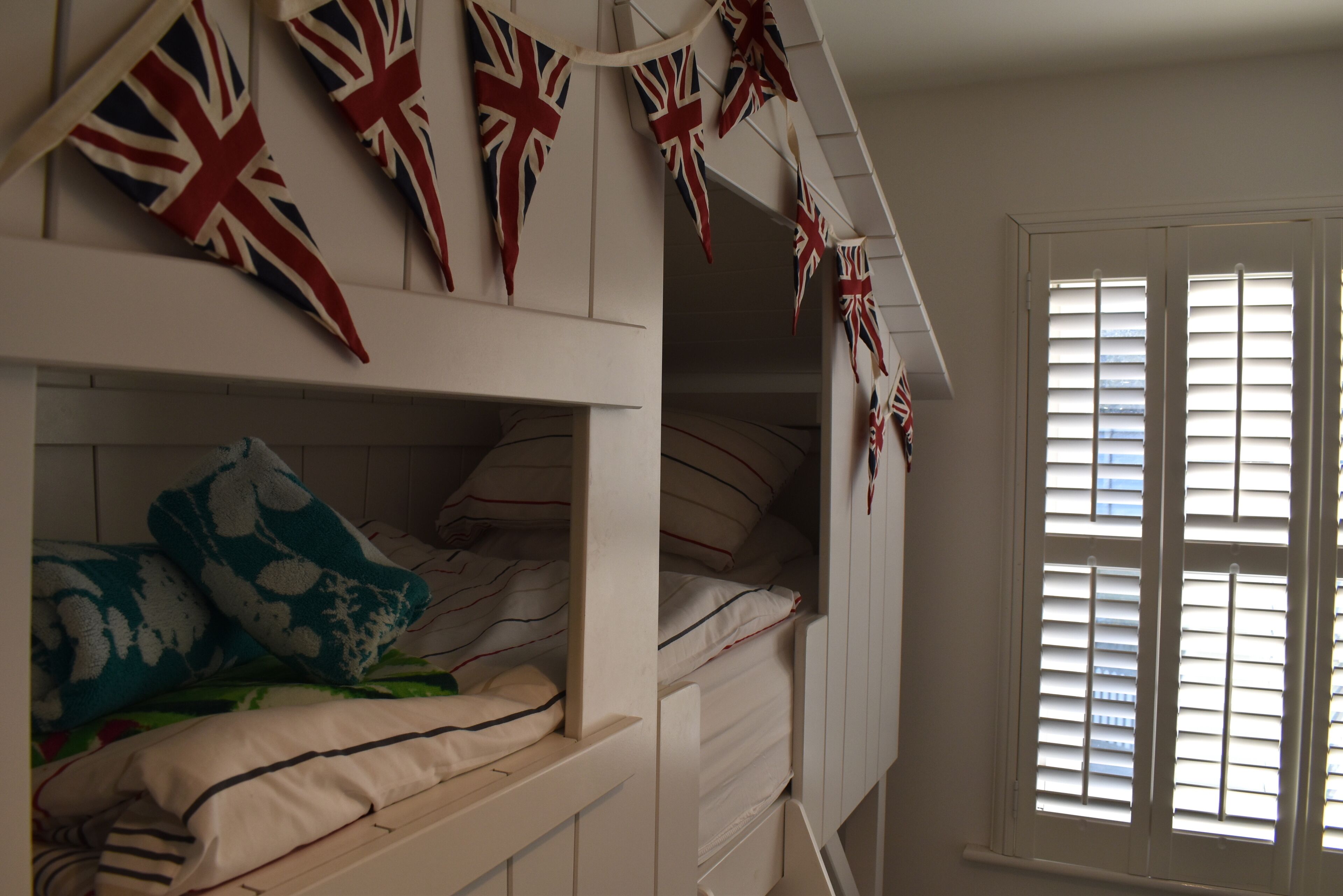 A room with bunk beds, a window with blinds, and British flags hanging above the beds.