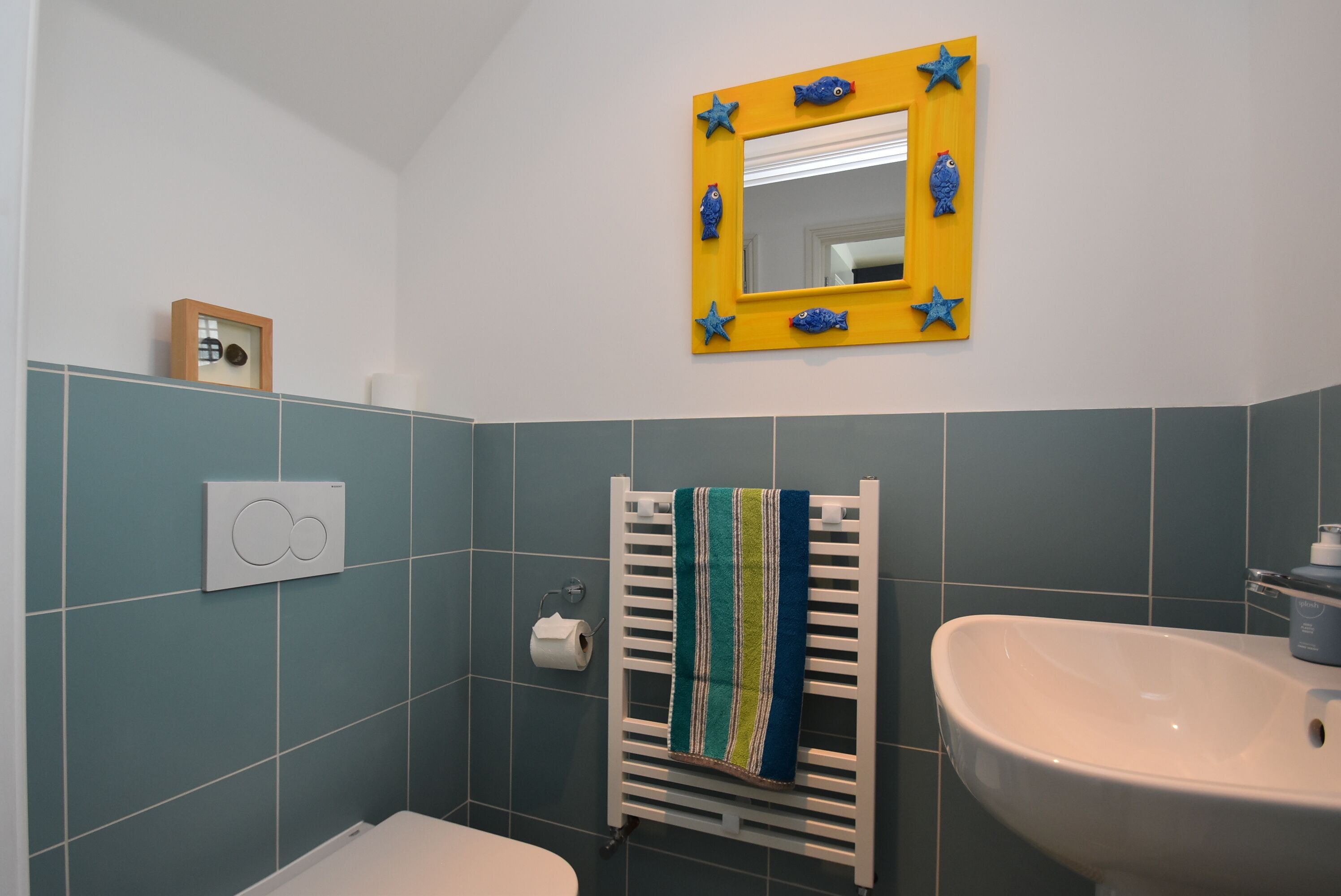 A bathroom with a white sink, a mirror with a yellow frame, and a towel rack with a striped towel.