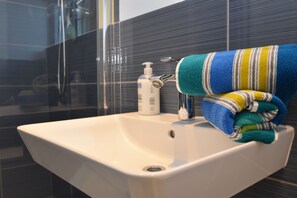 A bathroom with a white sink, a soap dispenser, and a towel on the edge.