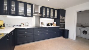 Una cocina moderna con armarios oscuros, horno empotrado y lavadora en una habitación contigua.
