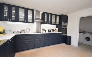 Una cocina moderna con armarios oscuros, horno empotrado y lavadora en una habitación contigua.