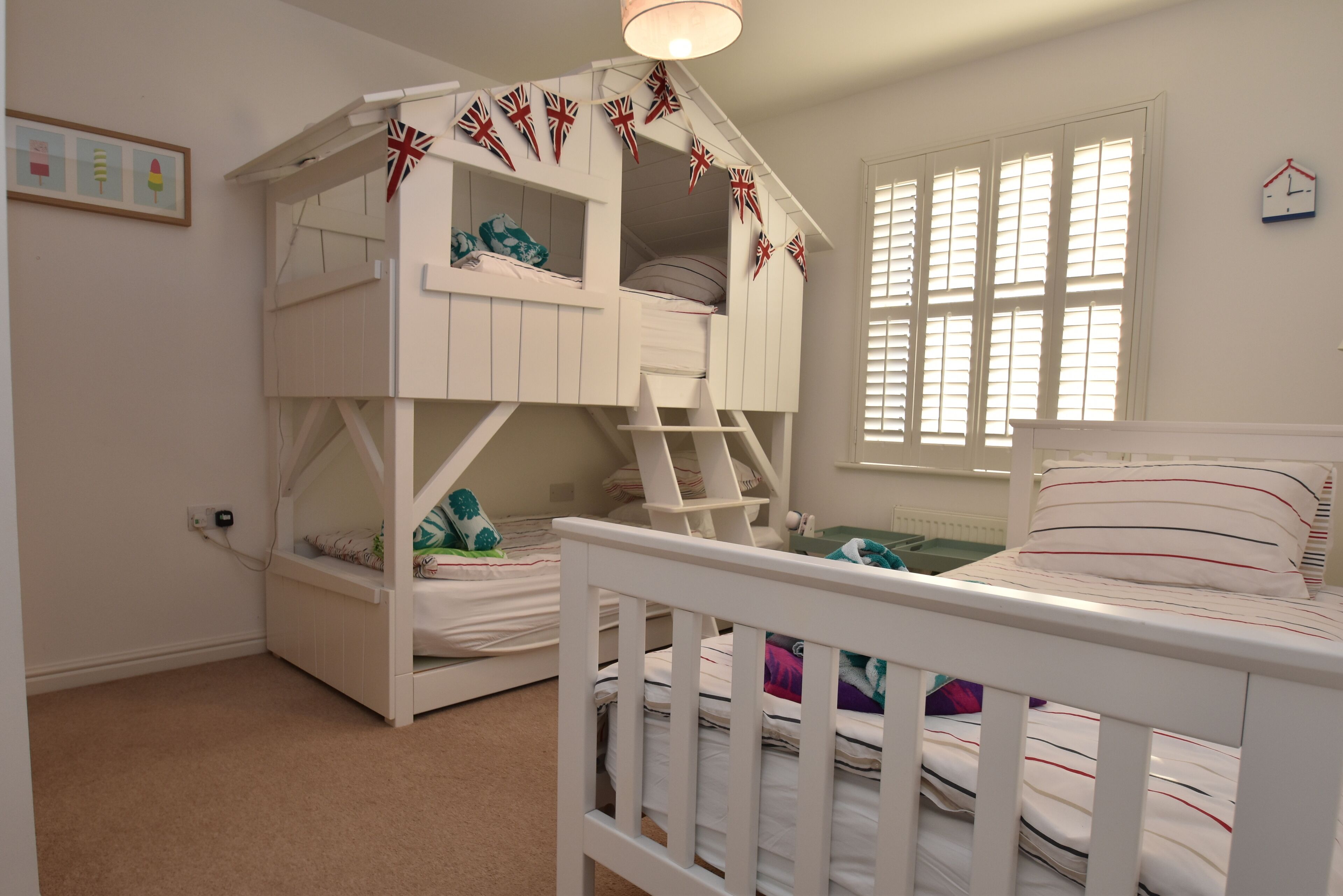A bunk bed room with a ladder, a window with blinds, and a wall clock.