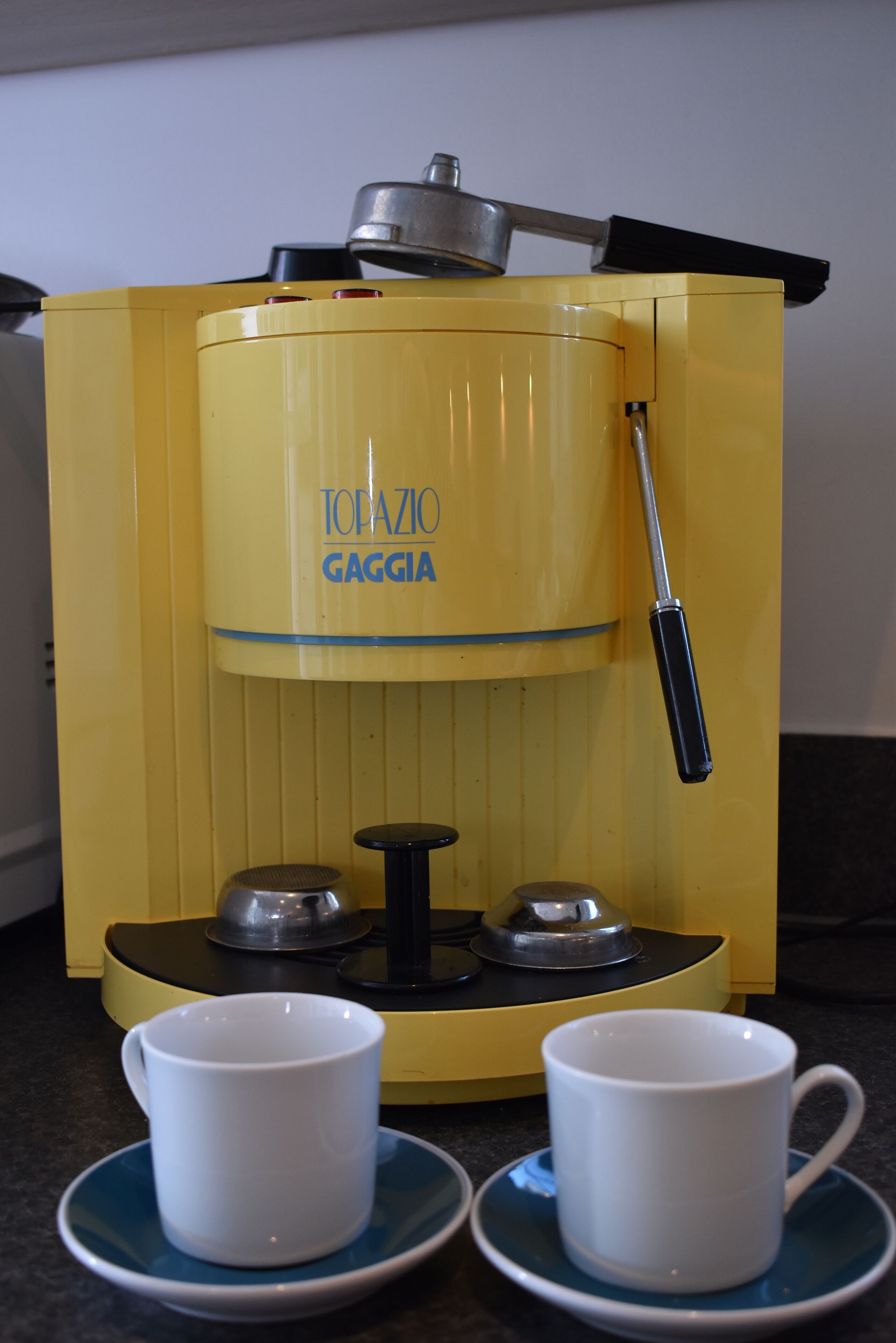 Une machine à café jaune avec deux tasses blanches posées sur des soucoupes.