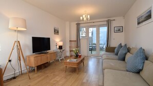 Una sala de estar moderna con un televisor de pantalla plana, muebles de madera, una mesa de centro con revistas y un sofá con cojines estampados.