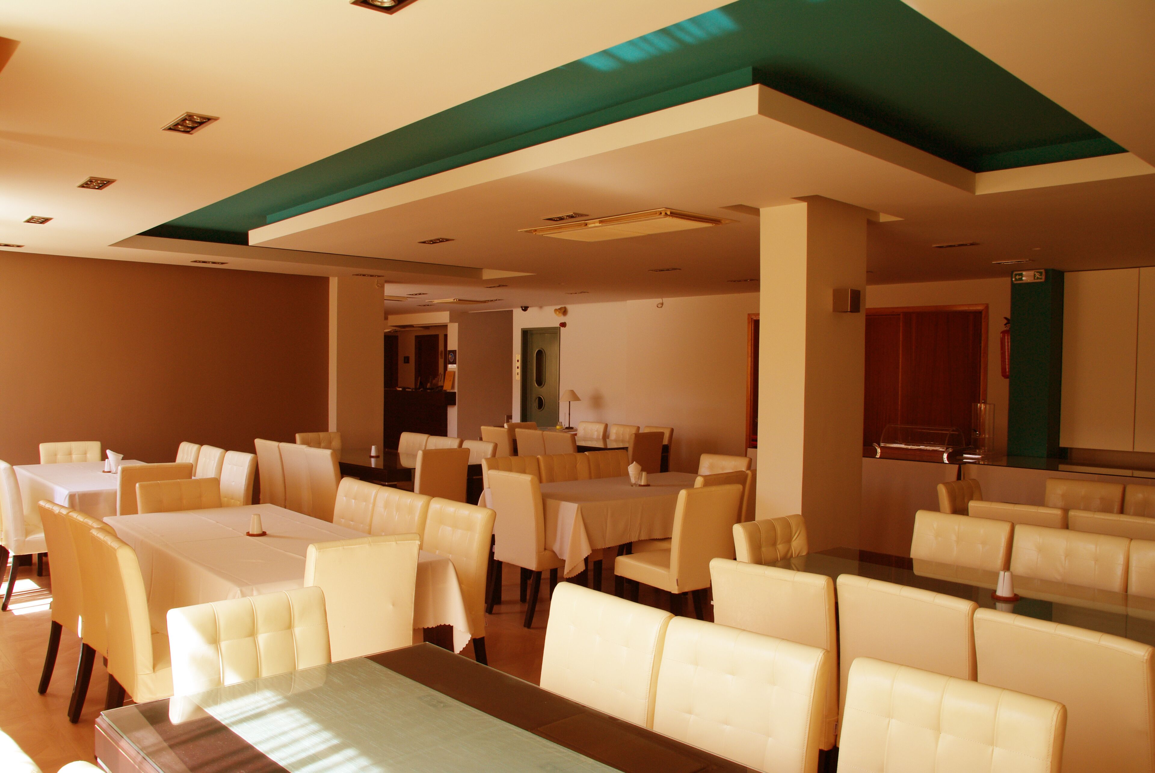 A spacious dining area with multiple tables and chairs, a high ceiling with recessed lighting, and a view of the adjacent kitchen area.