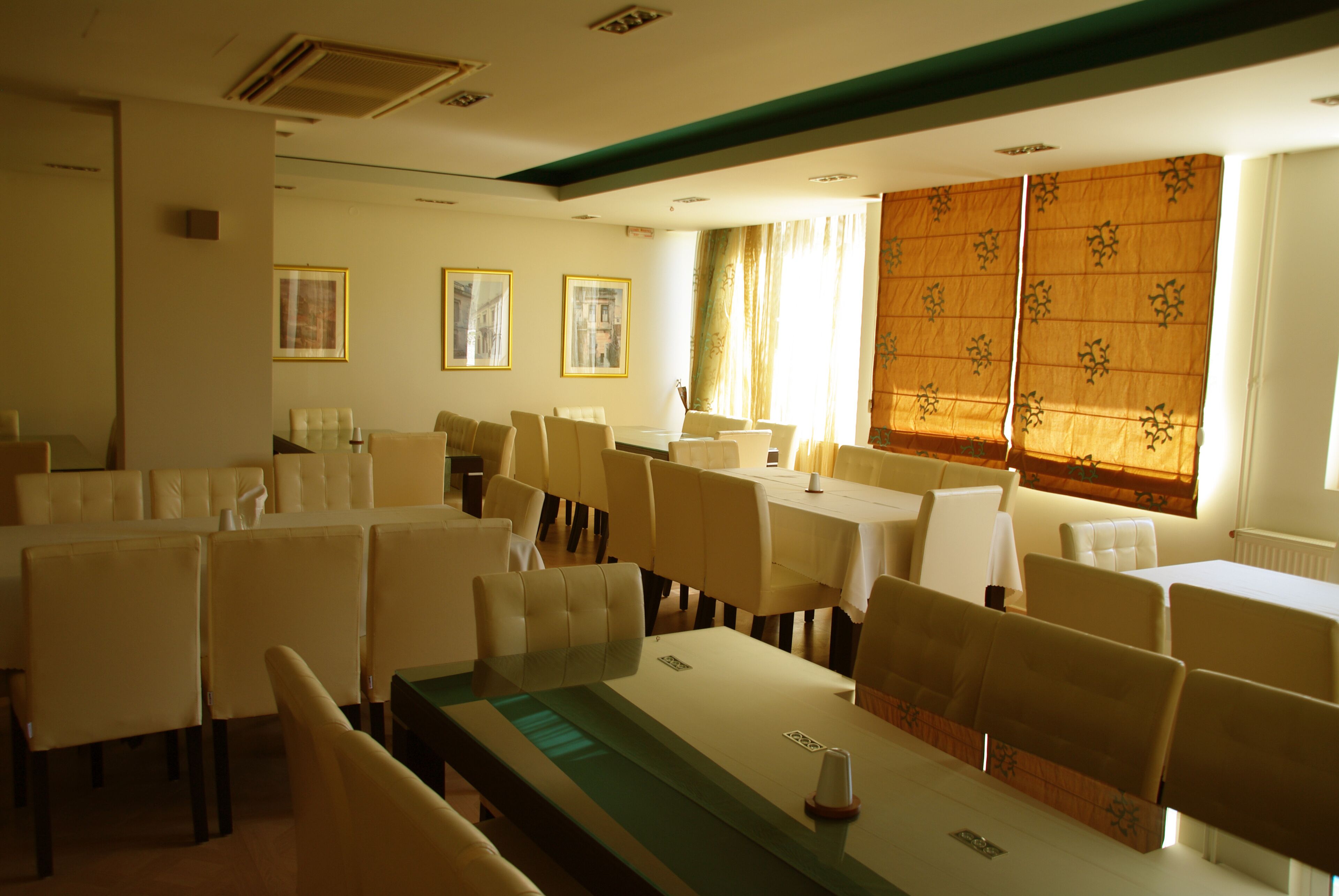 A dining area with multiple tables and chairs, framed pictures on the walls, and a large window with curtains.