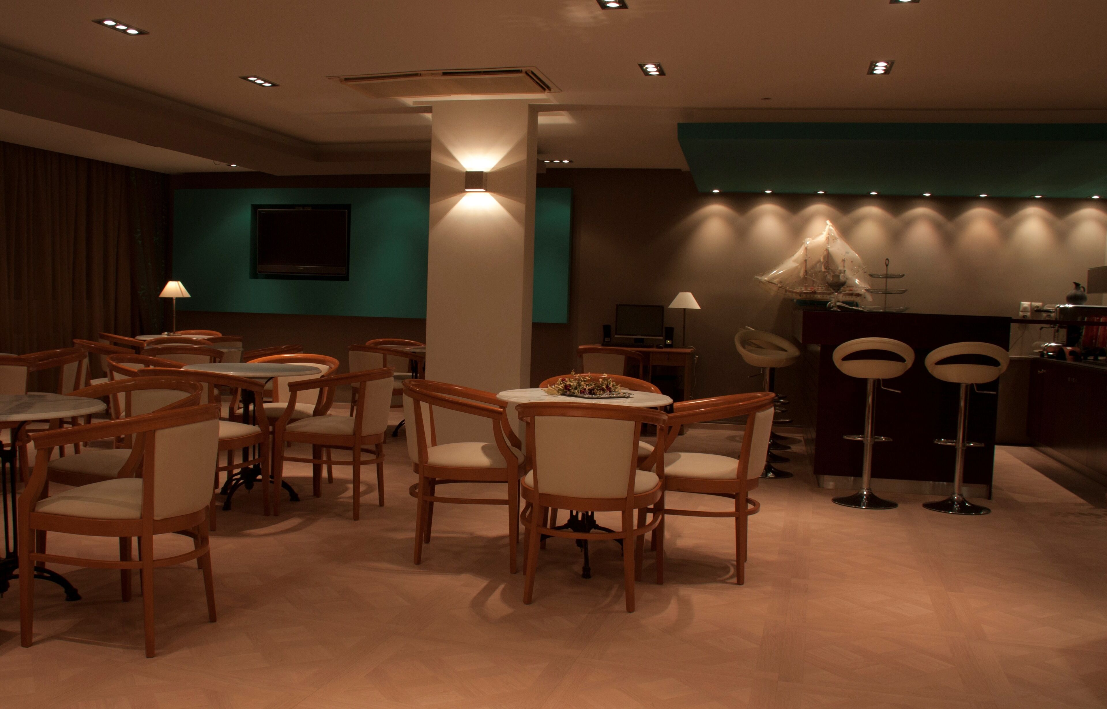 Un restaurante con mesas y sillas redondas, un televisor en la pared y una barra con taburetes.
