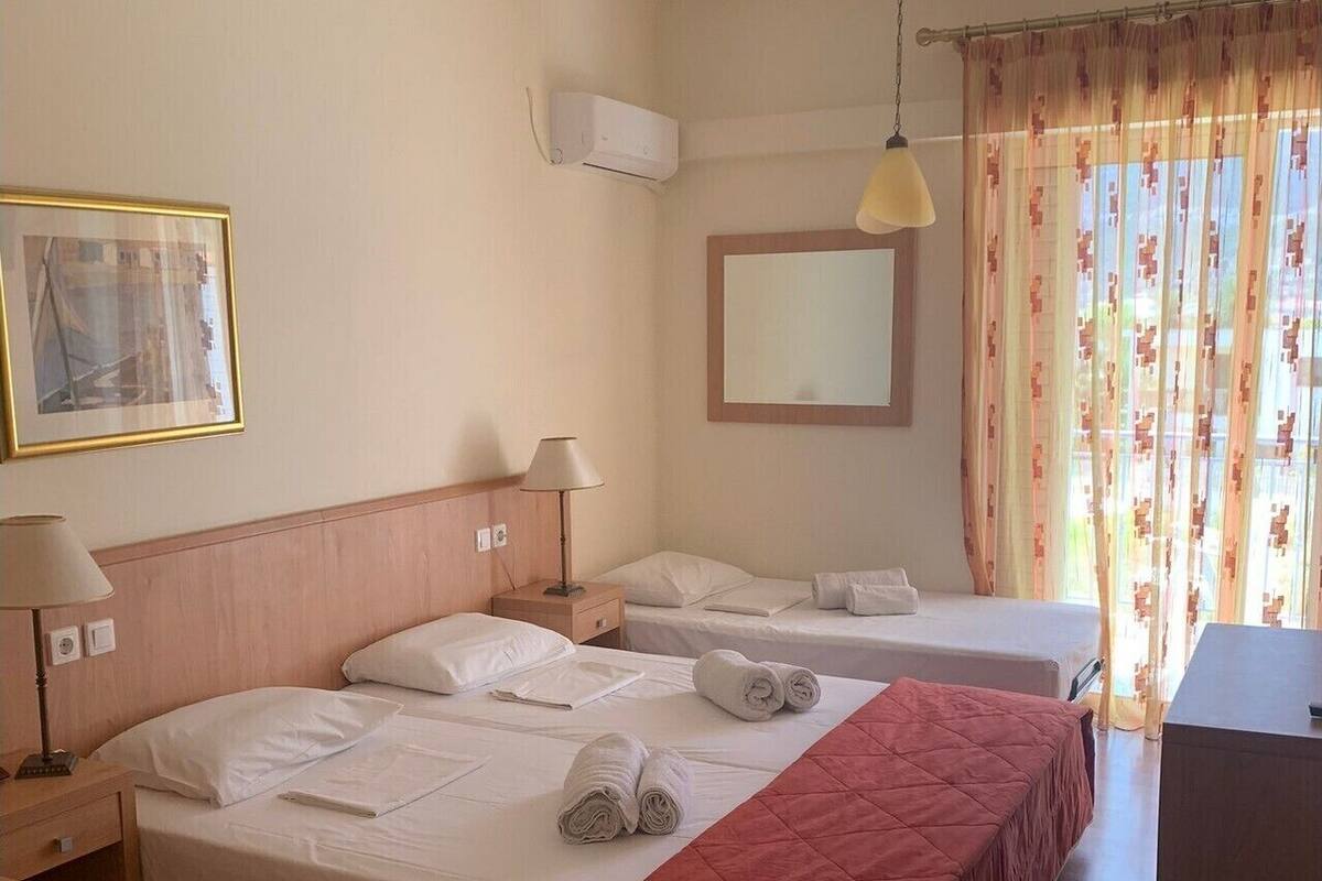 Habitación de hotel con dos camas, un escritorio, una silla, una lámpara, un espejo y una ventana con cortinas.