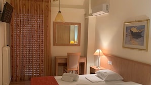 Habitación de hotel con cama, escritorio, silla, lámpara, un cuadro y ventana con cortinas.