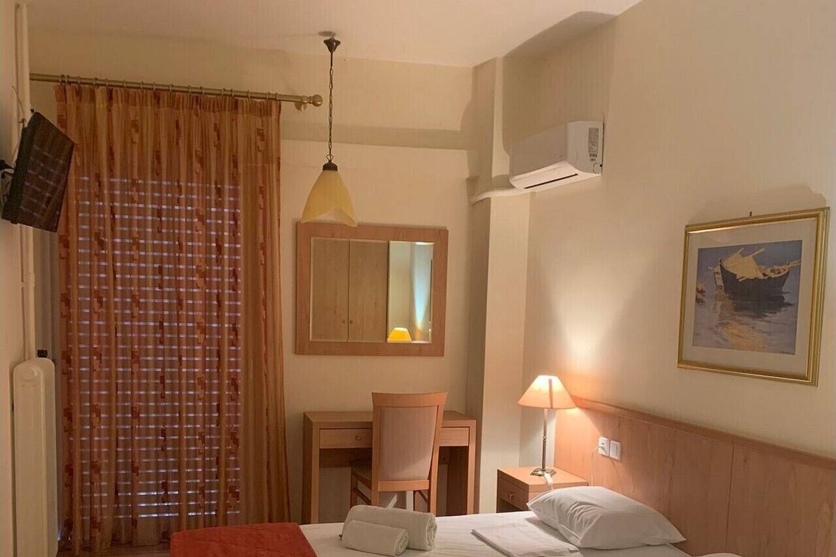 Habitación de hotel con cama, escritorio, silla, lámpara, un cuadro y ventana con cortinas.