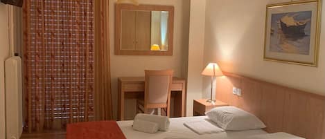 A hotel room with a bed, a desk, a chair, a lamp, a painting, and a window with curtains.