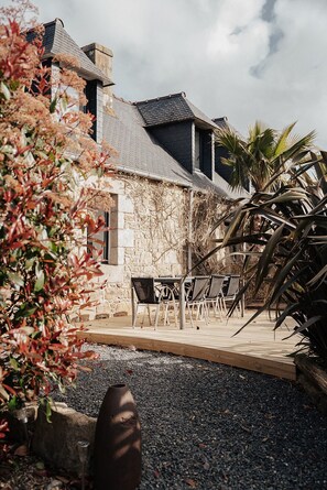 A stone building with a sloped roof, outdoor seating, and a palm tree.