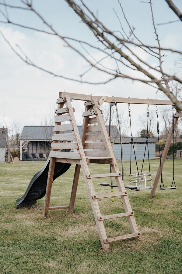 A wooden swing set with a slide and a ladder in a grassy yard.