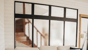 A room with a sectional sofa, a wooden coffee table, and a large window with a view of a staircase. - Stone farmhouse for 6 people with heated swimming pool (Trélévern)