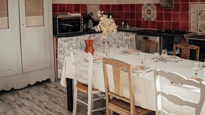 A dining area with a table set for four, a kitchen in the background, and a white cabinet with a window. - Stone farmhouse for 6 people with heated swimming pool (Trélévern)