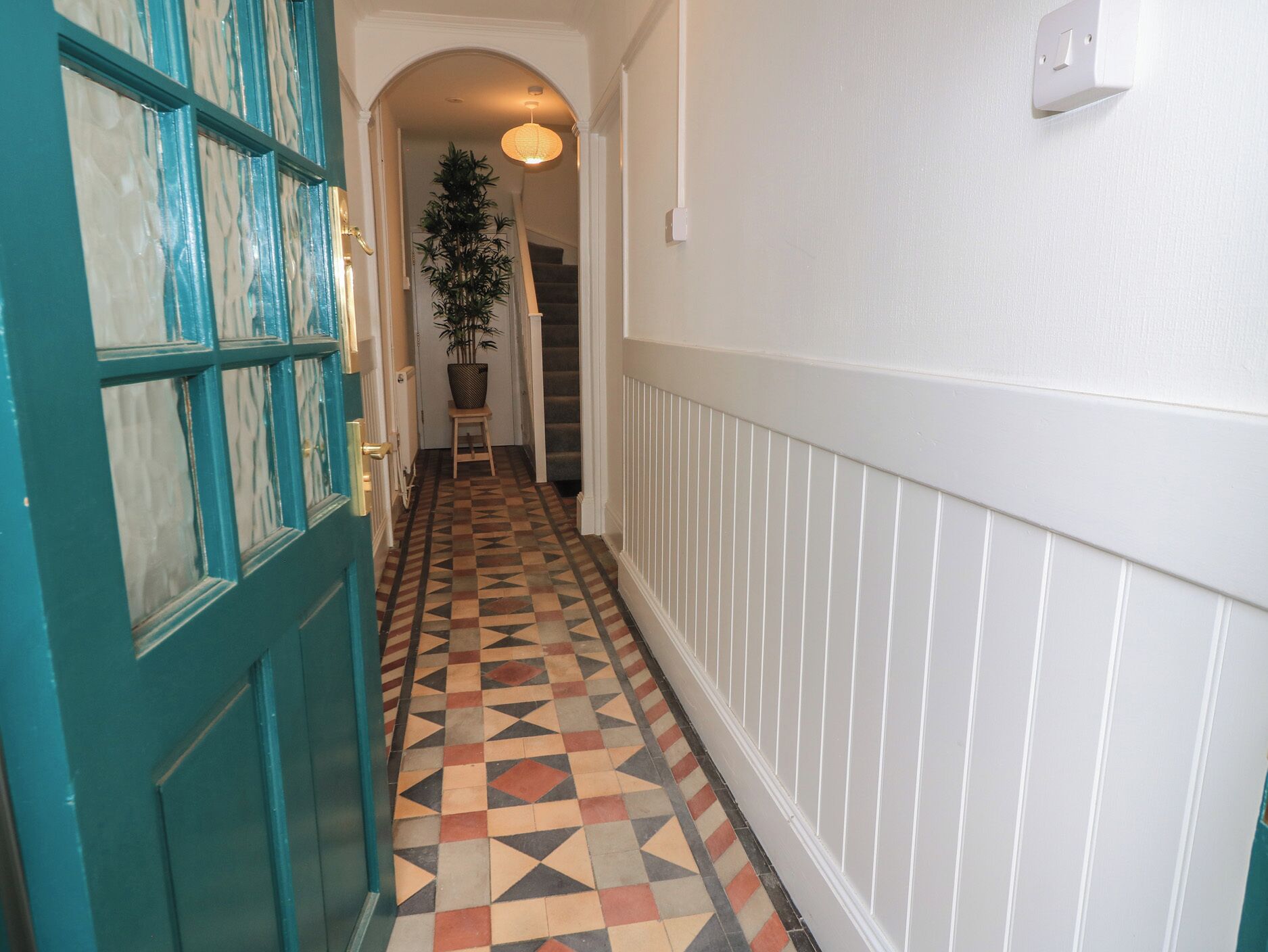 A hallway with a checkered floor, a teal door, and a staircase in the background.