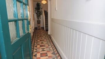 A hallway with a checkered floor, a teal door, and a staircase in the background.