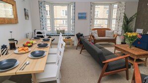 A dining area with a wooden table set for breakfast, a sofa, and a view of the city through large windows. - Still Waters (Swanage)