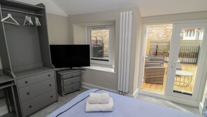 A bedroom with a bed, a TV, a dresser, and a balcony with outdoor furniture. - Still Waters (Swanage)