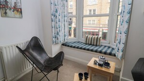 A cozy room with a black leather chair, a small wooden table with two mugs, a striped pillow on a window seat, and a radiator. - Still Waters (Swanage)