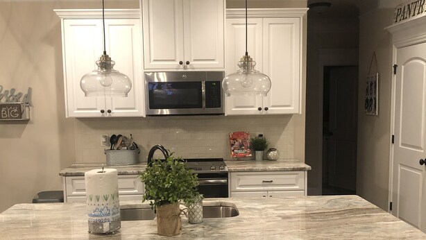 Una cocina con armarios blancos, una isla de mármol e iluminación colgante.