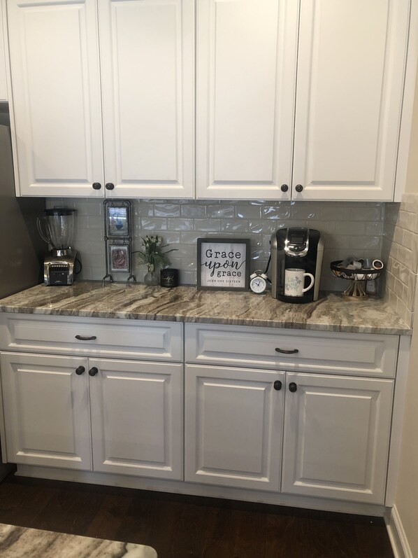 A kitchen with white cabinets, a marble countertop, a coffee maker, and a framed quote. - 5 miles from Masters. (Martinez)