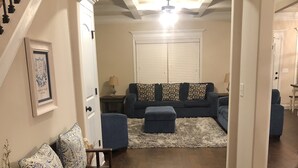 Un salón con un tapete azul oscuro, un conjunto de sofás y una escalera que lleva a otra habitación.