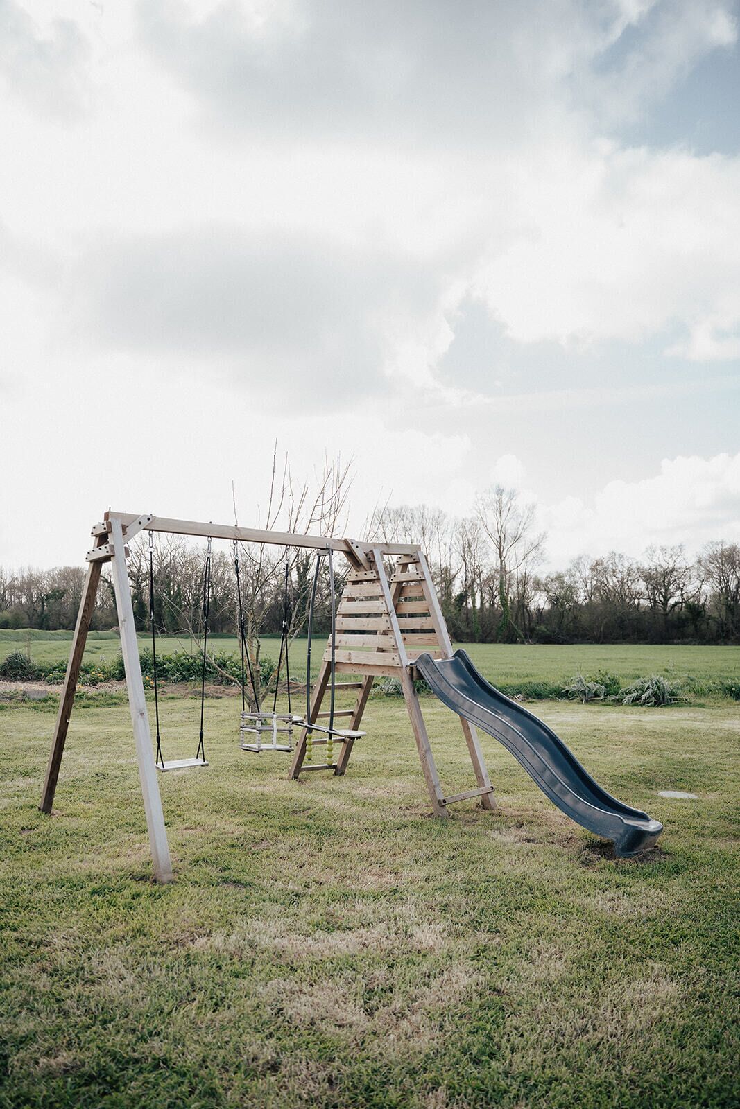 Ein Spielplatz mit Schaukeln, einer Rutsche und einer Kletterkonstruktion in einer grünen Wiese.
