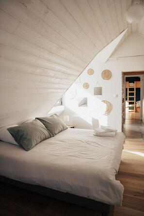 A bedroom with a sloped ceiling, a bed with pillows, a bedside table, and wall decorations. - Stone farmhouse for 10 people with heated swimming pool (Trélévern)