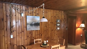 Uma sala de jantar de madeira com uma mesa, cadeiras, um lustre e um quadro na parede.