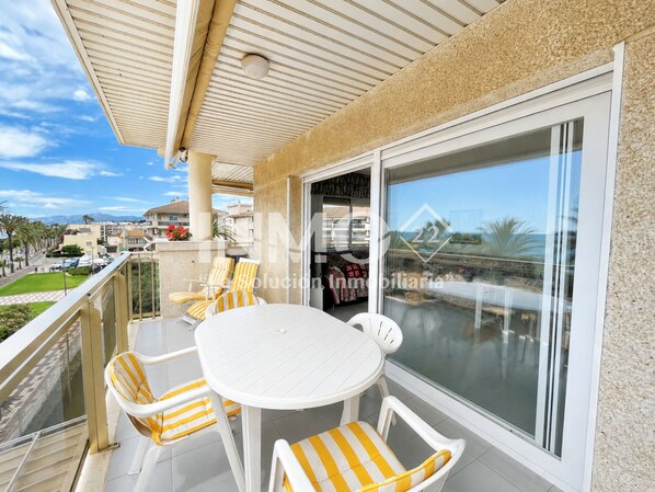 A balcony with a white table and chairs, a glass door, and a view of the cityscape.