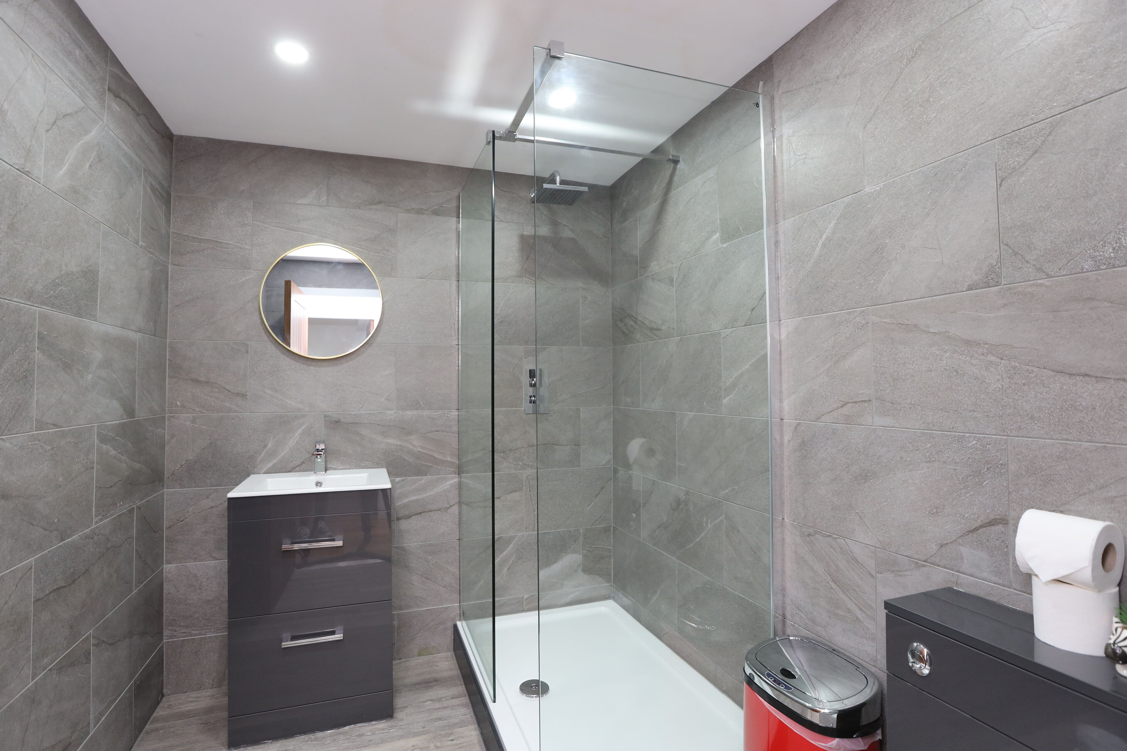 A modern bathroom with a glass-enclosed shower, a round mirror, a vanity with drawers, and a toilet.
