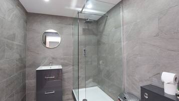 A modern bathroom with a glass-enclosed shower, a round mirror, a vanity with drawers, and a toilet.