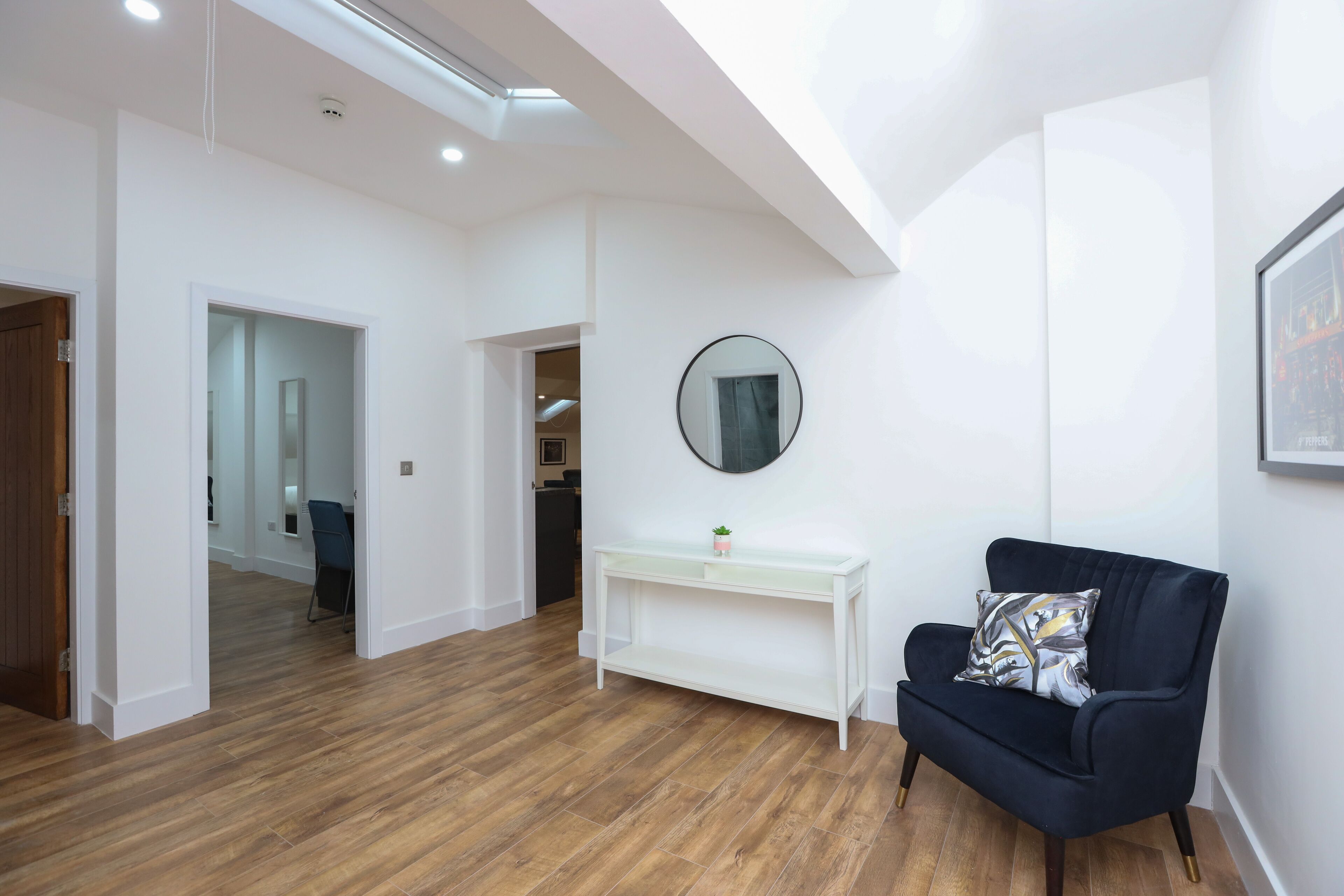 A modern living room with a dark blue armchair, a white console table, and a round mirror on the wall.